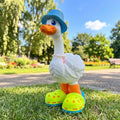 Prints & Giggles 3D white duck figurine wearing a blue bucket hat, pearl necklace, and neon green clogs in a park.