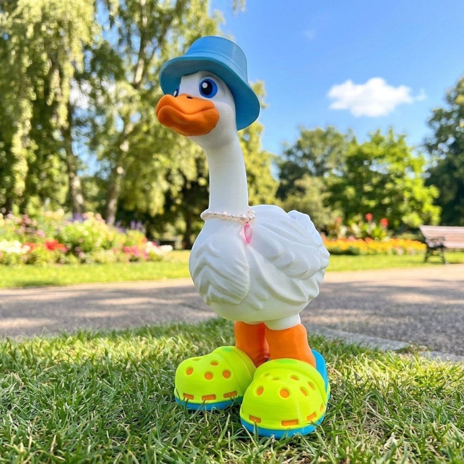 Prints & Giggles 3D white duck figurine wearing a blue bucket hat, pearl necklace, and neon green clogs in a park.
